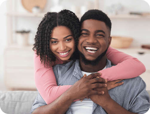 A woman hugging a man from behind, both are smiling.