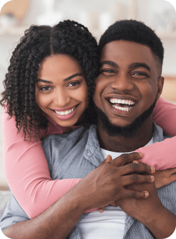 A woman hugging a man from behind, both are smiling.