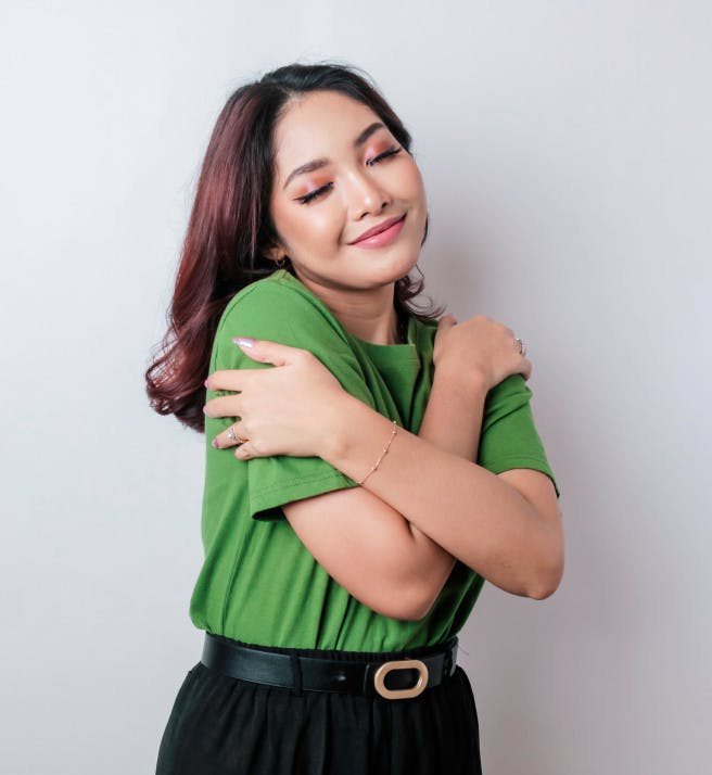 An woman hugging herself and smiling with her eyes closed.